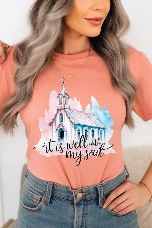 A woman wearing the "It Is Well With My Soul" graphic tee, featuring a grey color with an illustration of a church and the text "it is well with my soul.