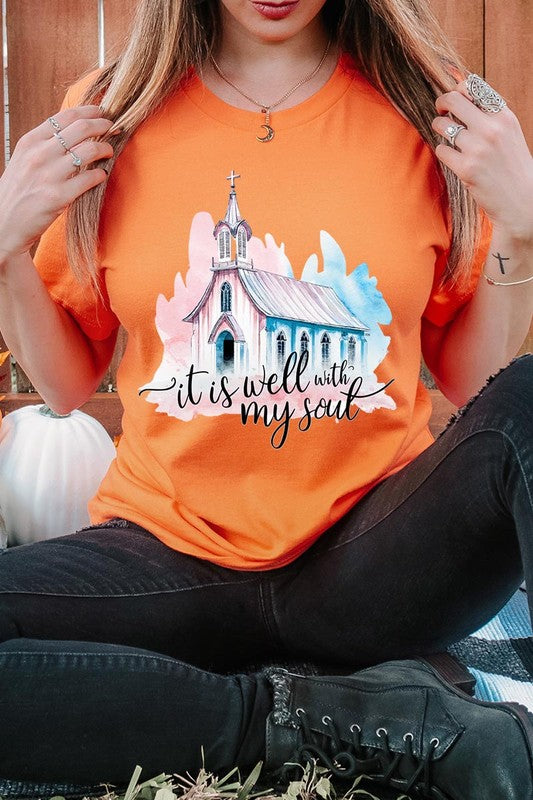 A woman wearing the "It Is Well With My Soul" graphic tee, featuring a grey color with an illustration of a church and the text "it is well with my soul.