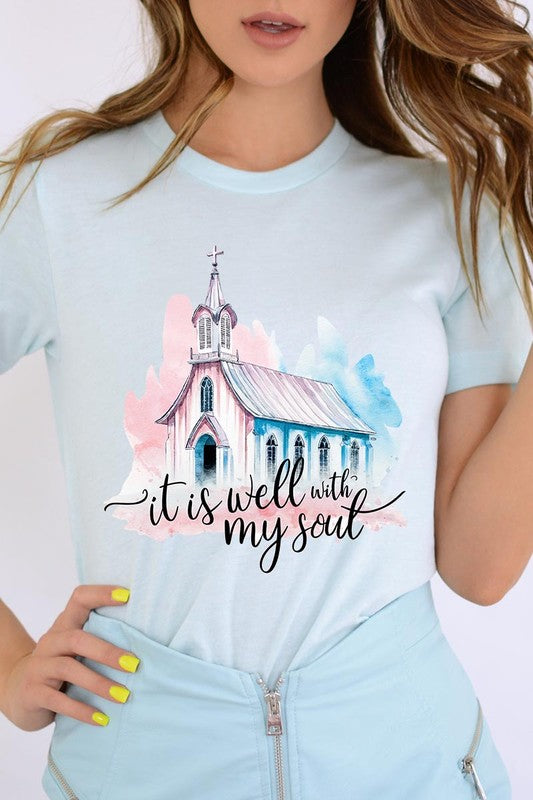 A woman wearing the "It Is Well With My Soul" graphic tee, featuring a grey color with an illustration of a church and the text "it is well with my soul.