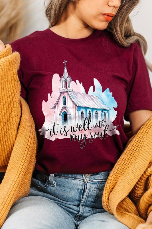 A woman wearing the "It Is Well With My Soul" graphic tee, featuring a grey color with an illustration of a church and the text "it is well with my soul.