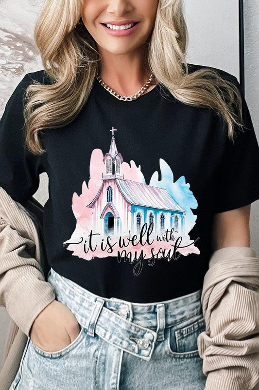 A woman wearing the "It Is Well With My Soul" graphic tee, featuring a grey color with an illustration of a church and the text "it is well with my soul.