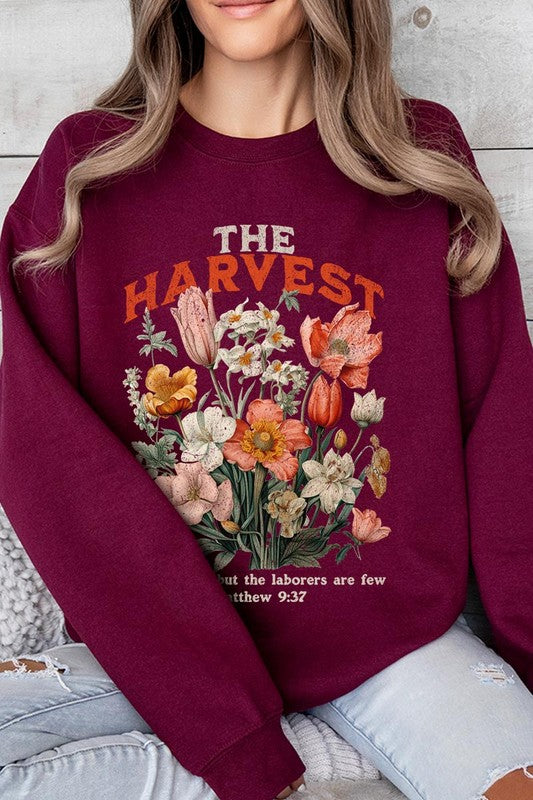 A person wearing 'The Harvest Christian Graphic Fleece Sweatshirt' in navy blue, adorned with floral graphics and the text "The Harvest" alongside "Matthew 9:37 - The harvest is plentiful, but the laborers are few," effortlessly combines style and comfort in this high-quality unisex crew neck.