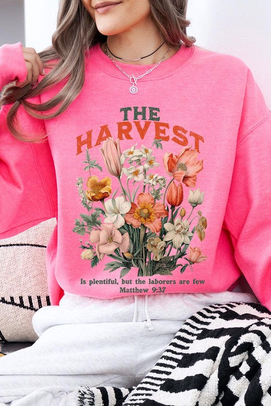 A person wearing 'The Harvest Christian Graphic Fleece Sweatshirt' in navy blue, adorned with floral graphics and the text "The Harvest" alongside "Matthew 9:37 - The harvest is plentiful, but the laborers are few," effortlessly combines style and comfort in this high-quality unisex crew neck.