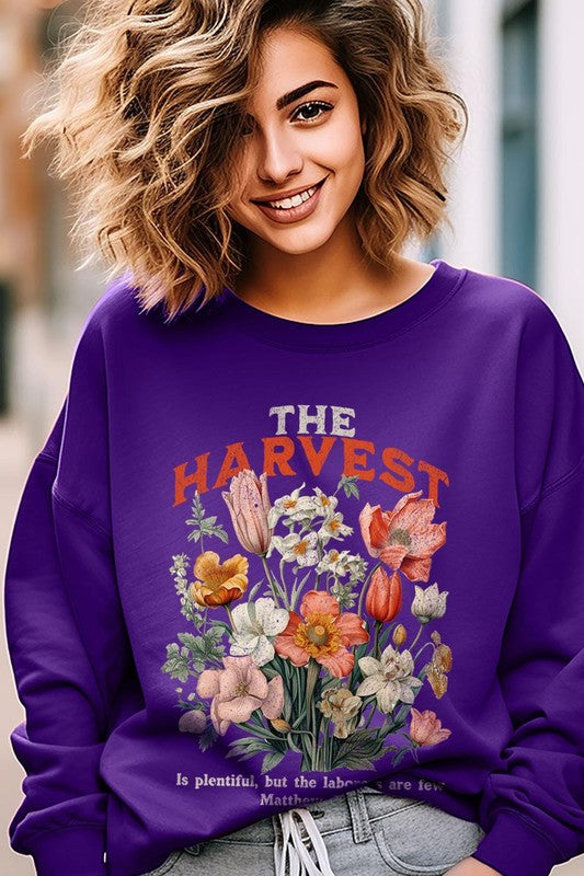 A person wearing 'The Harvest Christian Graphic Fleece Sweatshirt' in navy blue, adorned with floral graphics and the text "The Harvest" alongside "Matthew 9:37 - The harvest is plentiful, but the laborers are few," effortlessly combines style and comfort in this high-quality unisex crew neck.