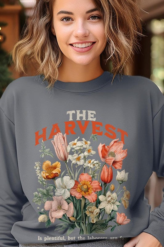 A person wearing 'The Harvest Christian Graphic Fleece Sweatshirt' in navy blue, adorned with floral graphics and the text "The Harvest" alongside "Matthew 9:37 - The harvest is plentiful, but the laborers are few," effortlessly combines style and comfort in this high-quality unisex crew neck.