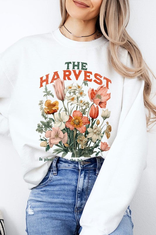 A person wearing 'The Harvest Christian Graphic Fleece Sweatshirt' in navy blue, adorned with floral graphics and the text "The Harvest" alongside "Matthew 9:37 - The harvest is plentiful, but the laborers are few," effortlessly combines style and comfort in this high-quality unisex crew neck.