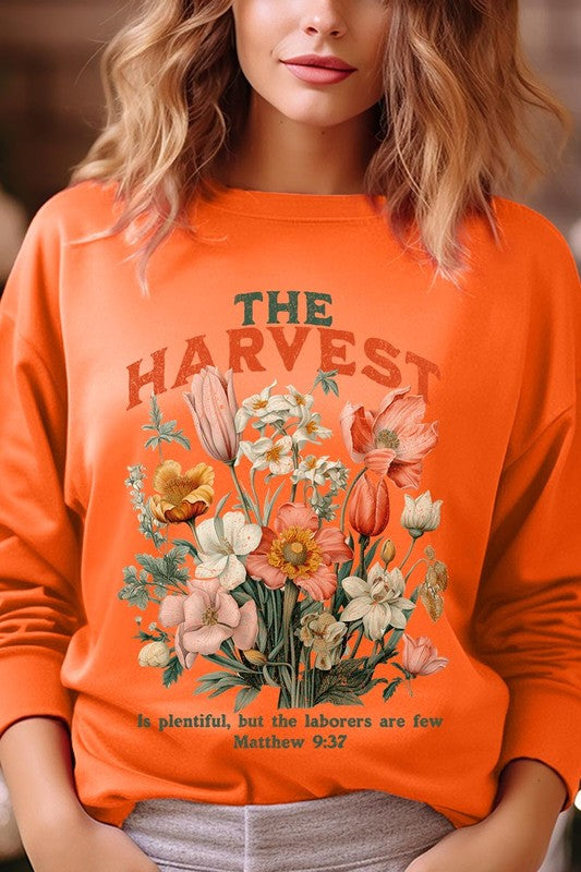 A person wearing 'The Harvest Christian Graphic Fleece Sweatshirt' in navy blue, adorned with floral graphics and the text "The Harvest" alongside "Matthew 9:37 - The harvest is plentiful, but the laborers are few," effortlessly combines style and comfort in this high-quality unisex crew neck.