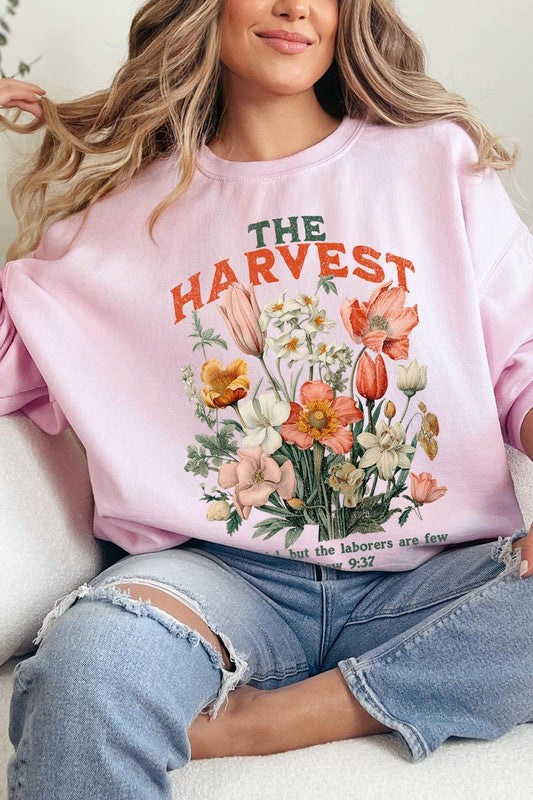 A person wearing 'The Harvest Christian Graphic Fleece Sweatshirt' in navy blue, adorned with floral graphics and the text "The Harvest" alongside "Matthew 9:37 - The harvest is plentiful, but the laborers are few," effortlessly combines style and comfort in this high-quality unisex crew neck.