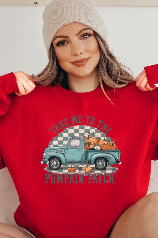 A woman with blonde hair wearing a "Take Me To The Pumpkin Patch" Fleece Sweatshirt stands in front of a vintage truck filled with pumpkins, holding a small device in her right hand.