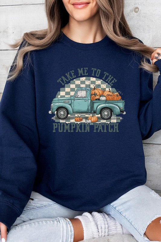 A woman with blonde hair wearing a "Take Me To The Pumpkin Patch" Fleece Sweatshirt stands in front of a vintage truck filled with pumpkins, holding a small device in her right hand.