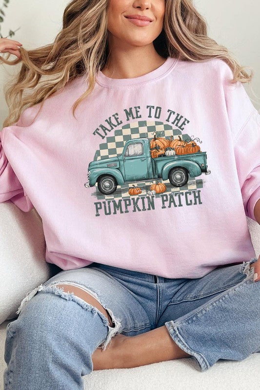 A woman with blonde hair wearing a "Take Me To The Pumpkin Patch" Fleece Sweatshirt stands in front of a vintage truck filled with pumpkins, holding a small device in her right hand.