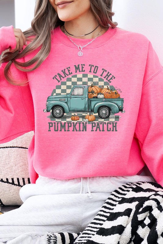 A woman with blonde hair wearing a "Take Me To The Pumpkin Patch" Fleece Sweatshirt stands in front of a vintage truck filled with pumpkins, holding a small device in her right hand.