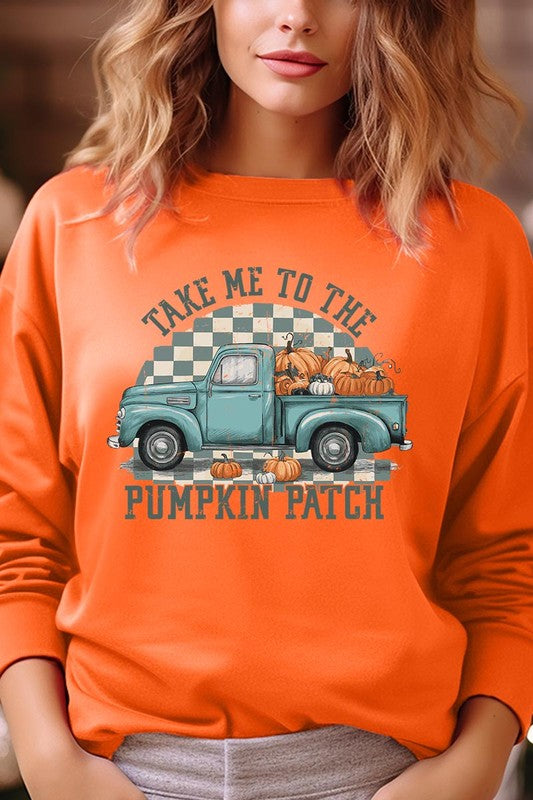 A woman with blonde hair wearing a "Take Me To The Pumpkin Patch" Fleece Sweatshirt stands in front of a vintage truck filled with pumpkins, holding a small device in her right hand.