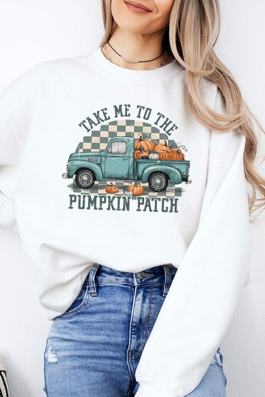 A woman with blonde hair wearing a "Take Me To The Pumpkin Patch" Fleece Sweatshirt stands in front of a vintage truck filled with pumpkins, holding a small device in her right hand.