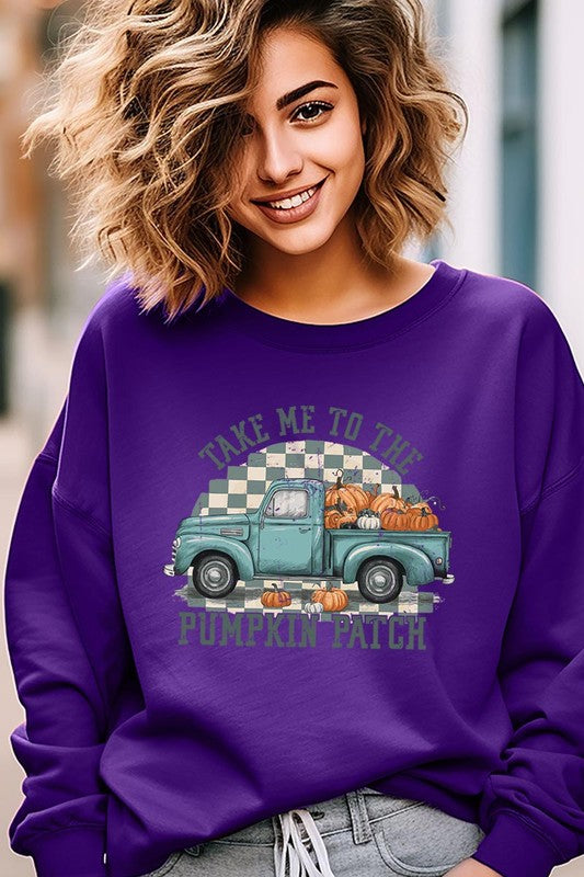 A woman with blonde hair wearing a "Take Me To The Pumpkin Patch" Fleece Sweatshirt stands in front of a vintage truck filled with pumpkins, holding a small device in her right hand.