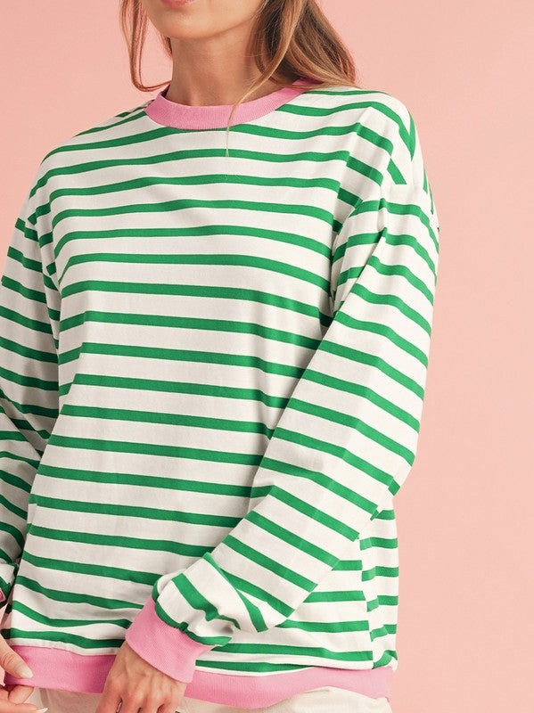 A person wearing the Cotton Stripe Drop Shoulder Sweatshirt, which features green stripes and pink cuffs, is facing away from the camera against a pink background.