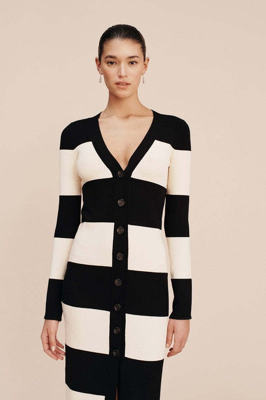 A person stands wearing the WOMEN FASHION CARDIGAN SWEATER DRESS, a long, black-and-white striped cardigan dress complete with buttons down the front and long sleeves.