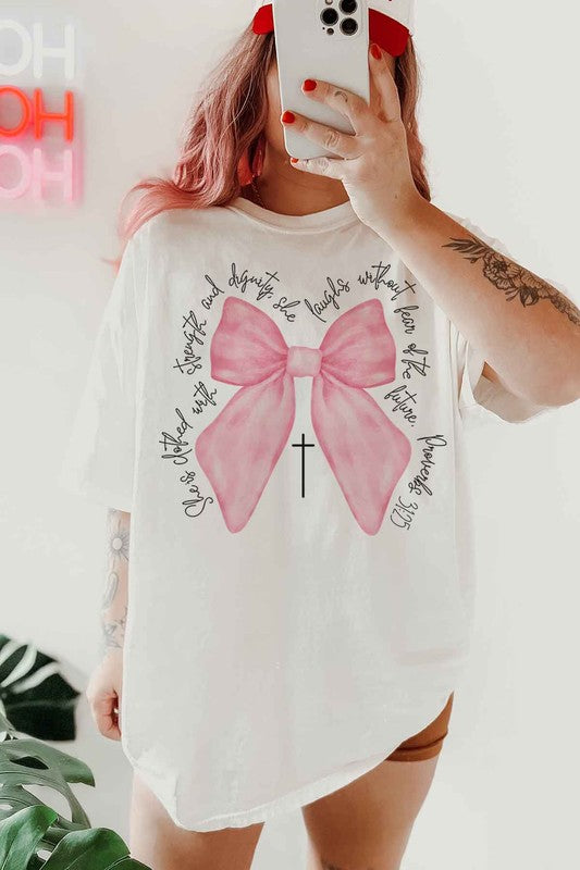 Person taking a mirror selfie wearing the PROVERBS PINK BOW CHRISTIAN OVERSIZED GRAPHIC TEE, made of premium cotton, featuring a large pink bow, a small cross below it, and cursive text around the design.