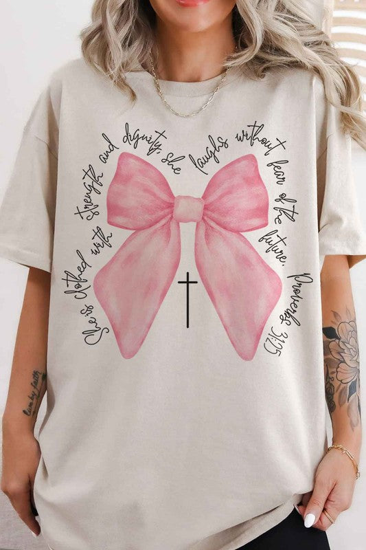 Person taking a mirror selfie wearing the PROVERBS PINK BOW CHRISTIAN OVERSIZED GRAPHIC TEE, made of premium cotton, featuring a large pink bow, a small cross below it, and cursive text around the design.