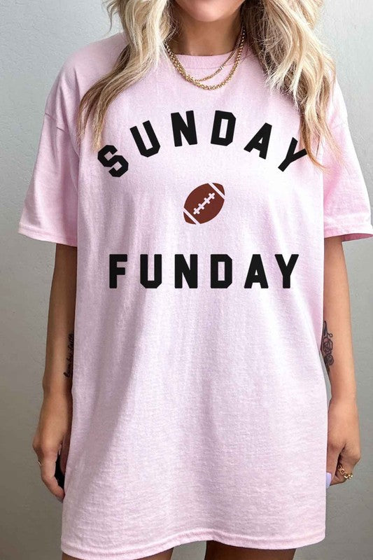 A person is wearing the SUNDAY FUN DAY FOOTBALL OVERSIZED GRAPHIC TEE made of premium cotton, featuring "Sunday Funday" and a small football graphic. They're holding a phone in front of their face, with part of a neon sign visible in the background—the perfect look for football game day.