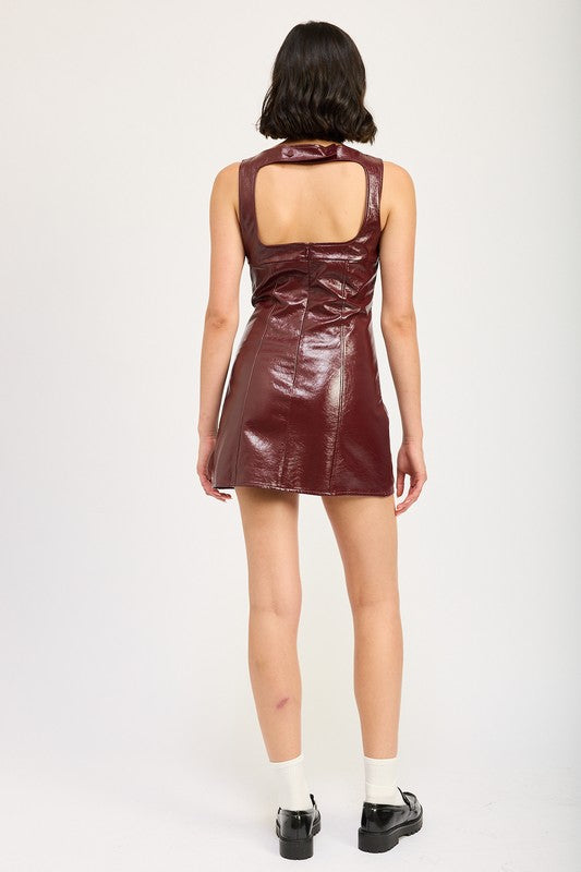 A woman wearing a sleeveless, SQUARED NECK LEATHER MINI DRESS WITH OPEN BACK in burgundy stands against a plain background. She is holding her sunglasses with one hand, the subtle sheen of her imported attire catching the light.