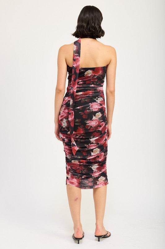 A woman wearing the SHIRRED FLORAL MINI DRESS WITH SCARF, a sleeveless, floral-print, form-fitting dress made of polyester, with a matching neck sash. She stands with one hand on her hip and pairs the outfit with black sandals. Available in size small.