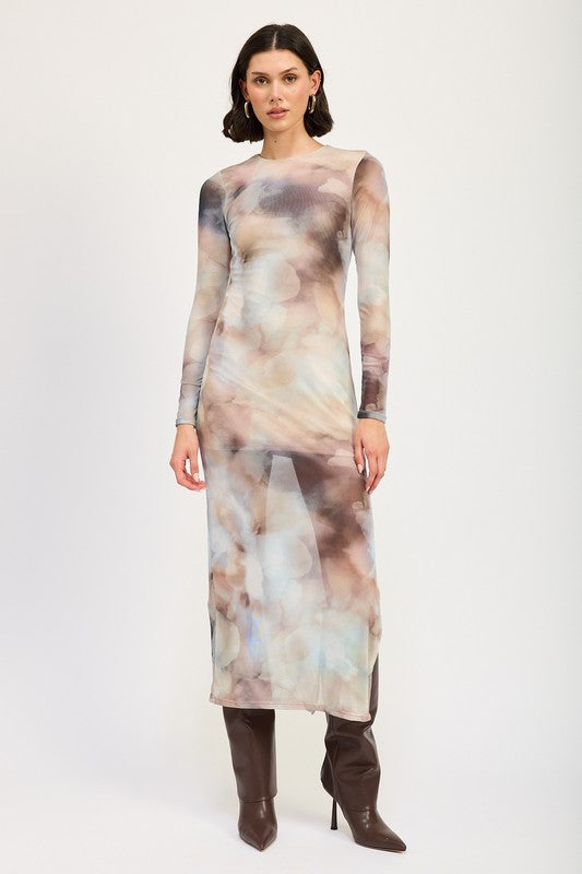 A person models a LONG SLEEVE MAXI DRESS WITH SLIT in size small, featuring sheer fabric and a watercolor print, paired with knee-high brown boots against a plain background. The model, standing at 5'9", showcases the dress which is made in the USA.