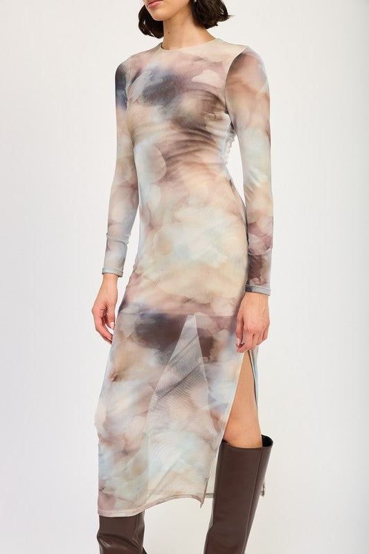 A person models a LONG SLEEVE MAXI DRESS WITH SLIT in size small, featuring sheer fabric and a watercolor print, paired with knee-high brown boots against a plain background. The model, standing at 5'9", showcases the dress which is made in the USA.