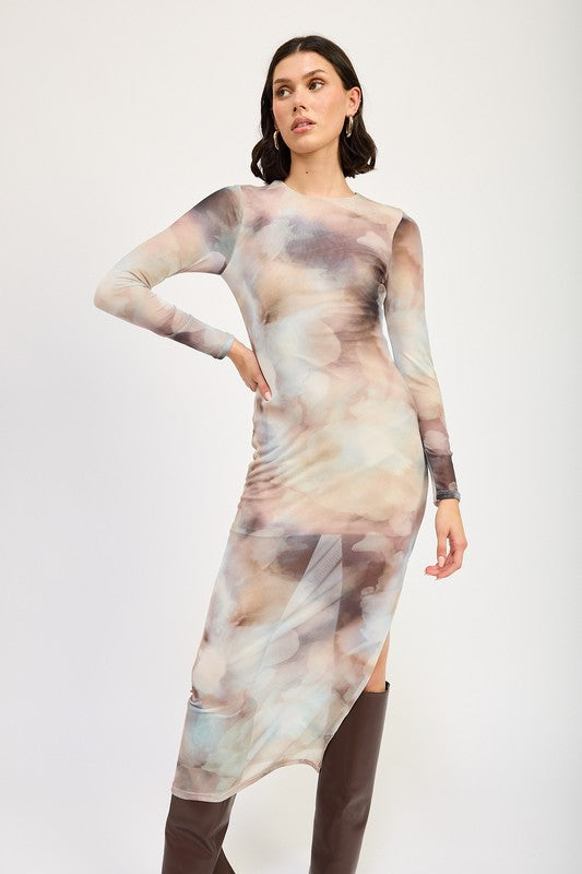 A person models a LONG SLEEVE MAXI DRESS WITH SLIT in size small, featuring sheer fabric and a watercolor print, paired with knee-high brown boots against a plain background. The model, standing at 5'9", showcases the dress which is made in the USA.