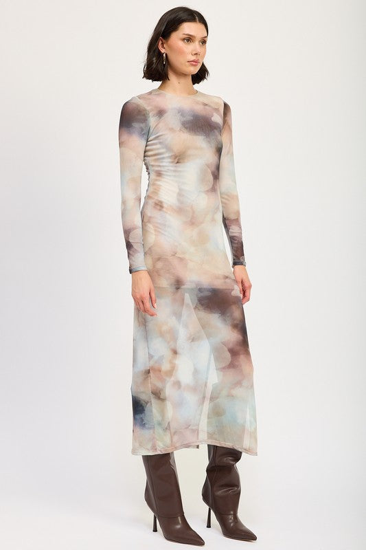 A person models a LONG SLEEVE MAXI DRESS WITH SLIT in size small, featuring sheer fabric and a watercolor print, paired with knee-high brown boots against a plain background. The model, standing at 5'9", showcases the dress which is made in the USA.