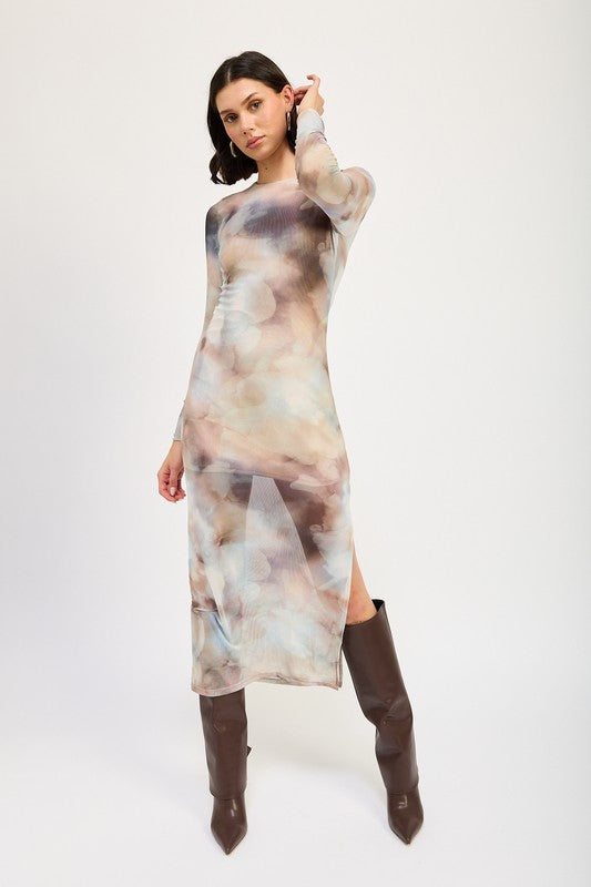 A person models a LONG SLEEVE MAXI DRESS WITH SLIT in size small, featuring sheer fabric and a watercolor print, paired with knee-high brown boots against a plain background. The model, standing at 5'9", showcases the dress which is made in the USA.