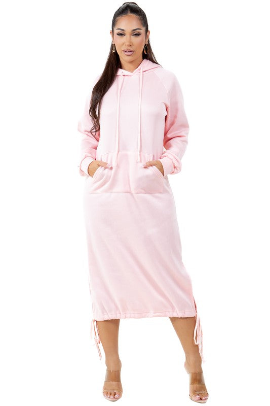 A woman wearing a WOMEN FASHION LONG MAXI HOODIE DRESS in light pink with long sleeves and a kanga pocket. She is standing and has one hand in her pocket.