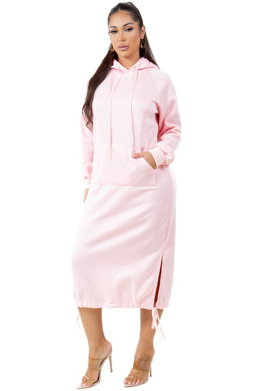 A woman wearing a WOMEN FASHION LONG MAXI HOODIE DRESS in light pink with long sleeves and a kanga pocket. She is standing and has one hand in her pocket.