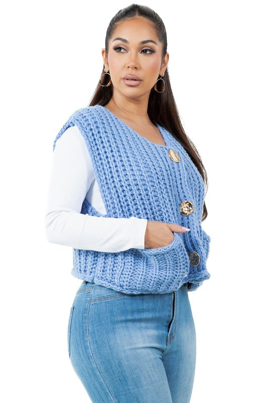 A woman posing with one hand in her pocket is wearing a WOMEN FASHION KNITWEAR VEST with large buttons over a white long sleeve shirt and blue jeans.