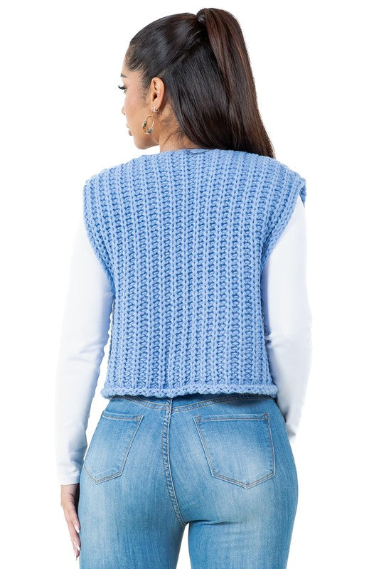 A woman posing with one hand in her pocket is wearing a WOMEN FASHION KNITWEAR VEST with large buttons over a white long sleeve shirt and blue jeans.