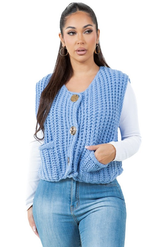 A woman posing with one hand in her pocket is wearing a WOMEN FASHION KNITWEAR VEST with large buttons over a white long sleeve shirt and blue jeans.