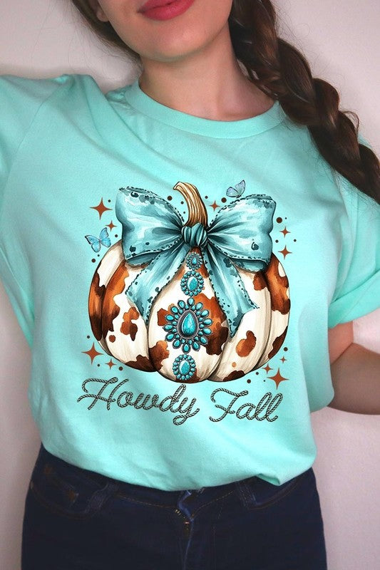 Person wearing the Howdy Fall Western Pumpkin Graphic Tee, featuring an illustrated pumpkin adorned with a blue bow and turquoise jewelry, along with the text "Howdy Fall." This beige unisex crew neck shirt pairs perfectly with their denim jacket.