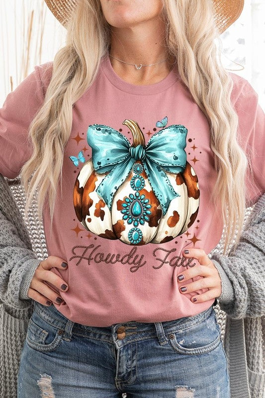 Person wearing the Howdy Fall Western Pumpkin Graphic Tee, featuring an illustrated pumpkin adorned with a blue bow and turquoise jewelry, along with the text "Howdy Fall." This beige unisex crew neck shirt pairs perfectly with their denim jacket.