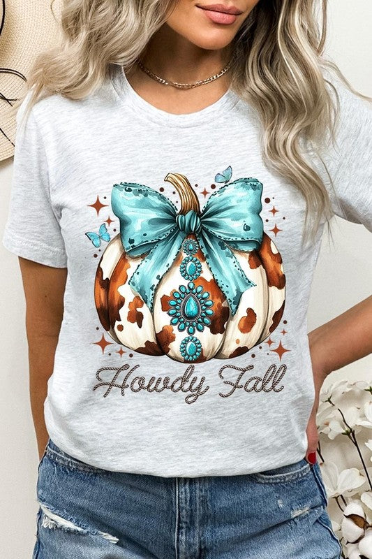 Person wearing the Howdy Fall Western Pumpkin Graphic Tee, featuring an illustrated pumpkin adorned with a blue bow and turquoise jewelry, along with the text "Howdy Fall." This beige unisex crew neck shirt pairs perfectly with their denim jacket.