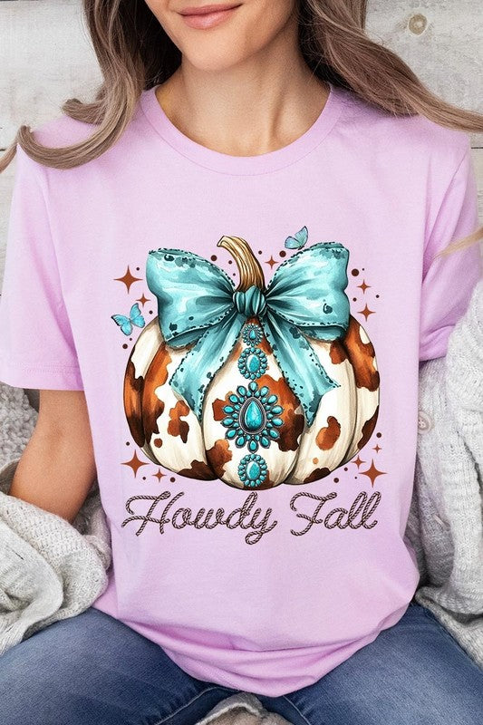 Person wearing the Howdy Fall Western Pumpkin Graphic Tee, featuring an illustrated pumpkin adorned with a blue bow and turquoise jewelry, along with the text "Howdy Fall." This beige unisex crew neck shirt pairs perfectly with their denim jacket.