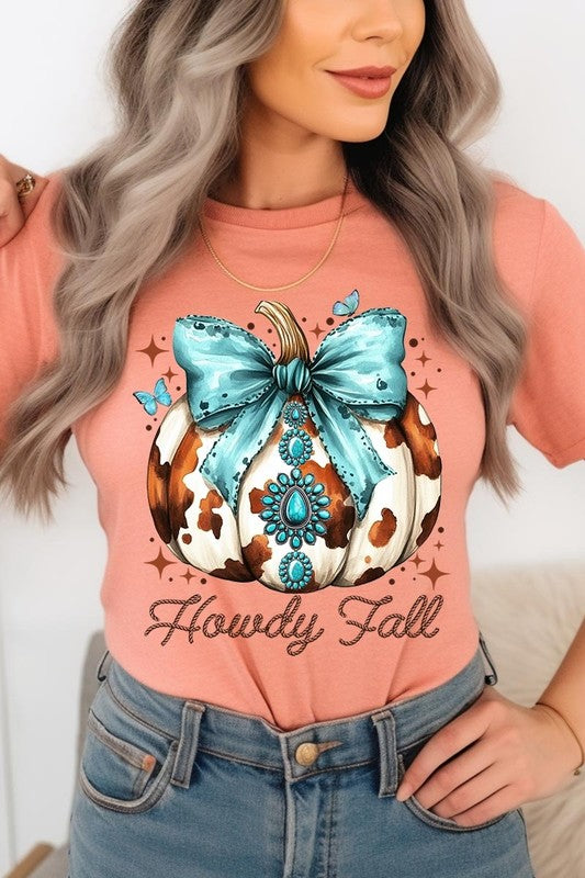 Person wearing the Howdy Fall Western Pumpkin Graphic Tee, featuring an illustrated pumpkin adorned with a blue bow and turquoise jewelry, along with the text "Howdy Fall." This beige unisex crew neck shirt pairs perfectly with their denim jacket.