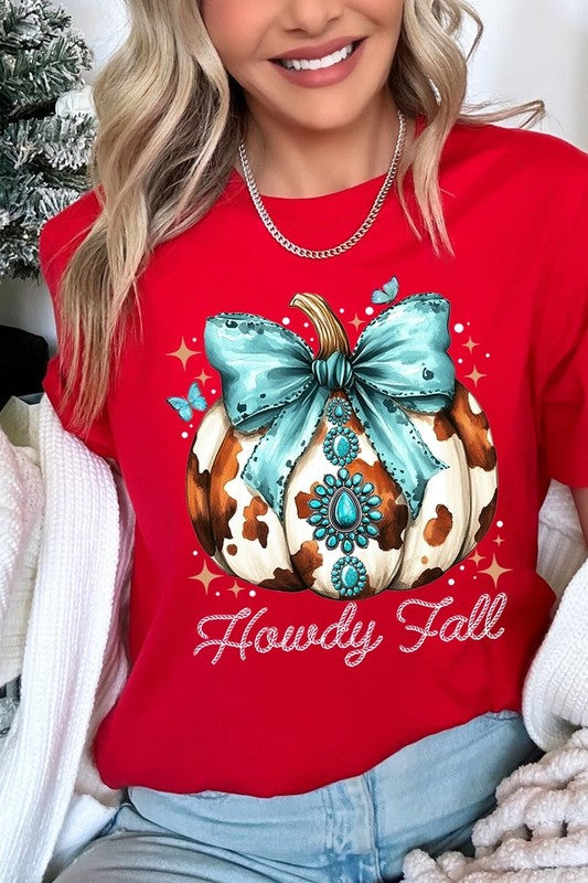 Person wearing the Howdy Fall Western Pumpkin Graphic Tee, featuring an illustrated pumpkin adorned with a blue bow and turquoise jewelry, along with the text "Howdy Fall." This beige unisex crew neck shirt pairs perfectly with their denim jacket.