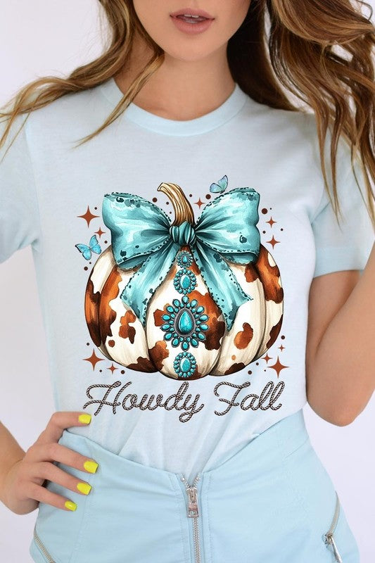 Person wearing the Howdy Fall Western Pumpkin Graphic Tee, featuring an illustrated pumpkin adorned with a blue bow and turquoise jewelry, along with the text "Howdy Fall." This beige unisex crew neck shirt pairs perfectly with their denim jacket.