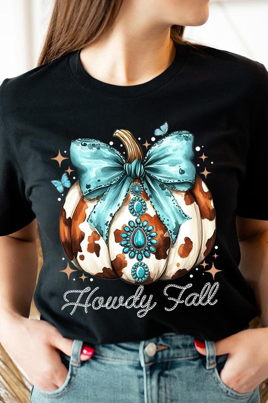 Person wearing the Howdy Fall Western Pumpkin Graphic Tee, featuring an illustrated pumpkin adorned with a blue bow and turquoise jewelry, along with the text "Howdy Fall." This beige unisex crew neck shirt pairs perfectly with their denim jacket.