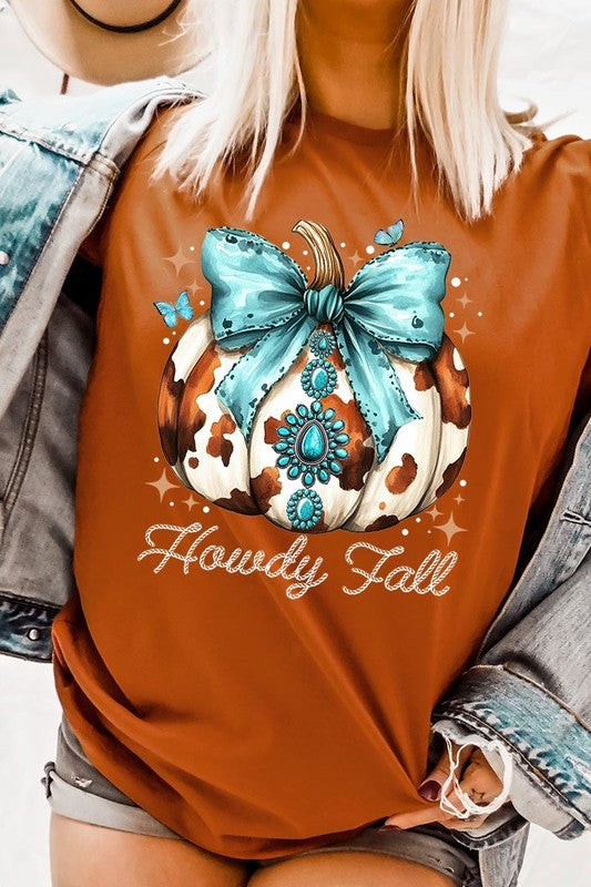 Person wearing the Howdy Fall Western Pumpkin Graphic Tee, featuring an illustrated pumpkin adorned with a blue bow and turquoise jewelry, along with the text "Howdy Fall." This beige unisex crew neck shirt pairs perfectly with their denim jacket.