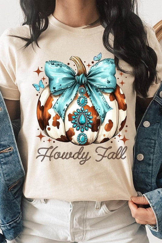 Person wearing the Howdy Fall Western Pumpkin Graphic Tee, featuring an illustrated pumpkin adorned with a blue bow and turquoise jewelry, along with the text "Howdy Fall." This beige unisex crew neck shirt pairs perfectly with their denim jacket.