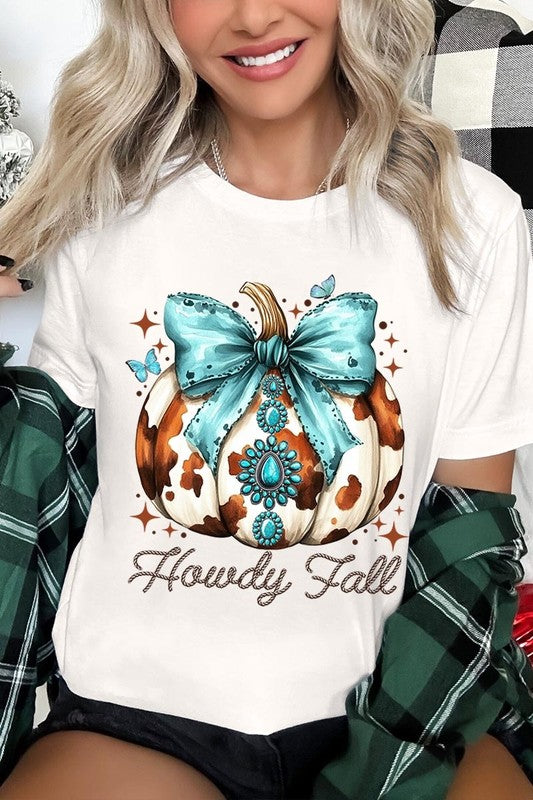 Person wearing the Howdy Fall Western Pumpkin Graphic Tee, featuring an illustrated pumpkin adorned with a blue bow and turquoise jewelry, along with the text "Howdy Fall." This beige unisex crew neck shirt pairs perfectly with their denim jacket.