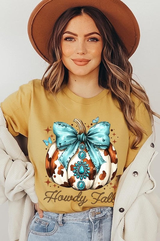 Person wearing the Howdy Fall Western Pumpkin Graphic Tee, featuring an illustrated pumpkin adorned with a blue bow and turquoise jewelry, along with the text "Howdy Fall." This beige unisex crew neck shirt pairs perfectly with their denim jacket.