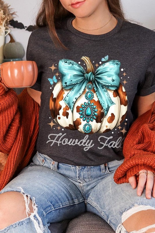 Person wearing the Howdy Fall Western Pumpkin Graphic Tee, featuring an illustrated pumpkin adorned with a blue bow and turquoise jewelry, along with the text "Howdy Fall." This beige unisex crew neck shirt pairs perfectly with their denim jacket.