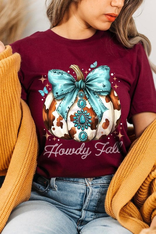 Person wearing the Howdy Fall Western Pumpkin Graphic Tee, featuring an illustrated pumpkin adorned with a blue bow and turquoise jewelry, along with the text "Howdy Fall." This beige unisex crew neck shirt pairs perfectly with their denim jacket.